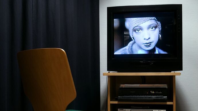 A chair in front of a TV showing the face of a woman in black and white