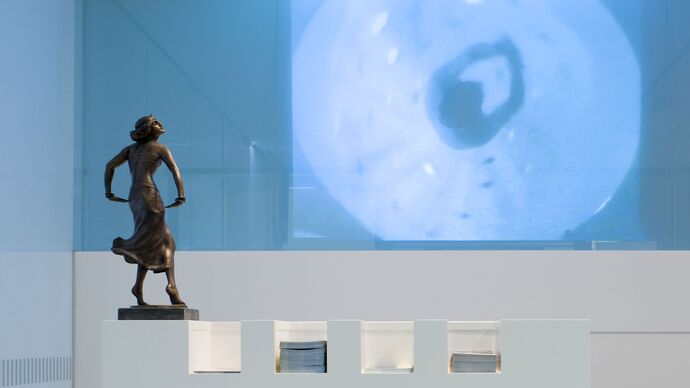 Eine kleine Bronzefigur, die eine Tänzerin zeigt, vor einer blauen Wand